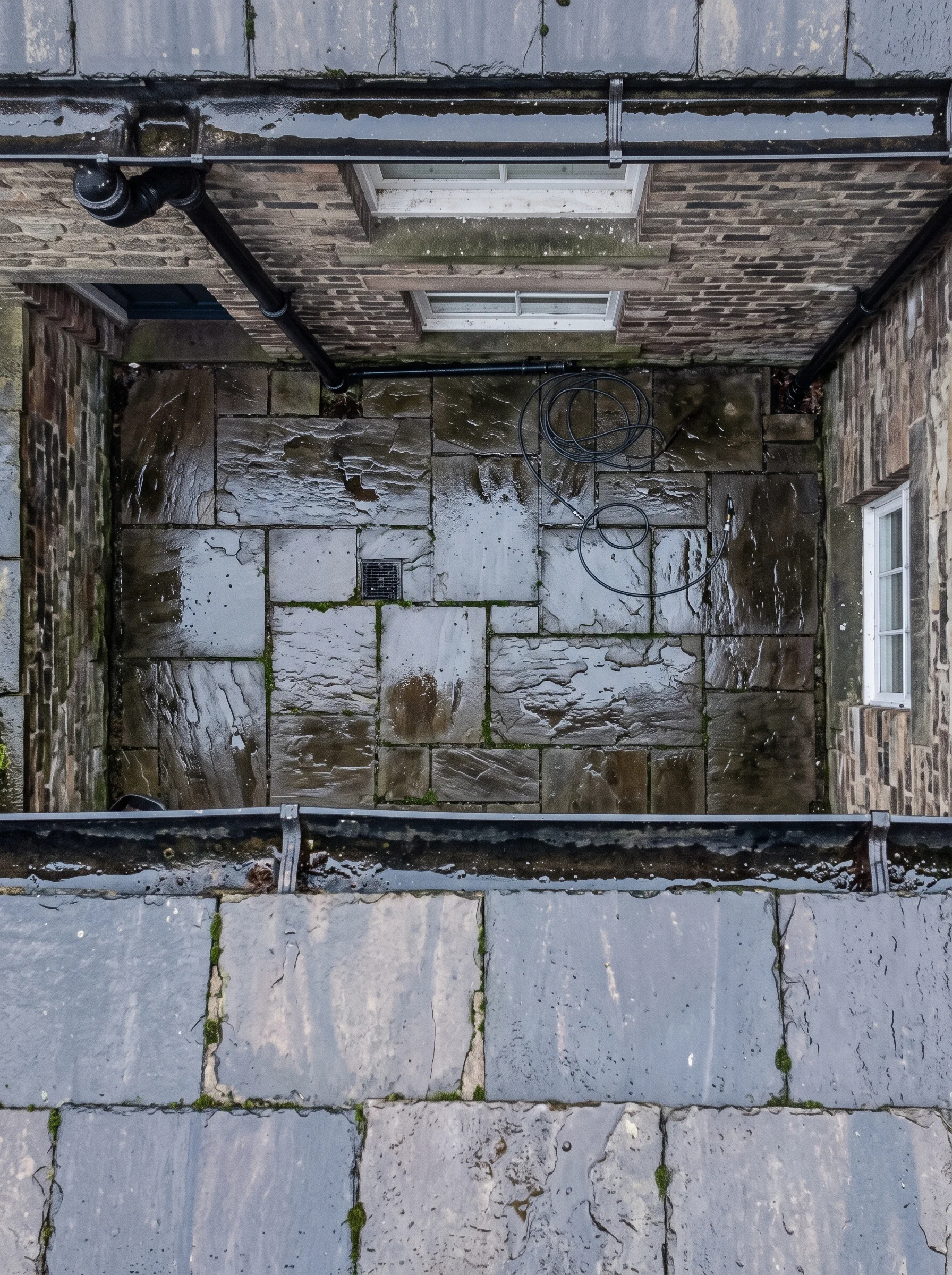 An overhead view from gutter height looking down at a wet flagstone yard with a coiled hose.